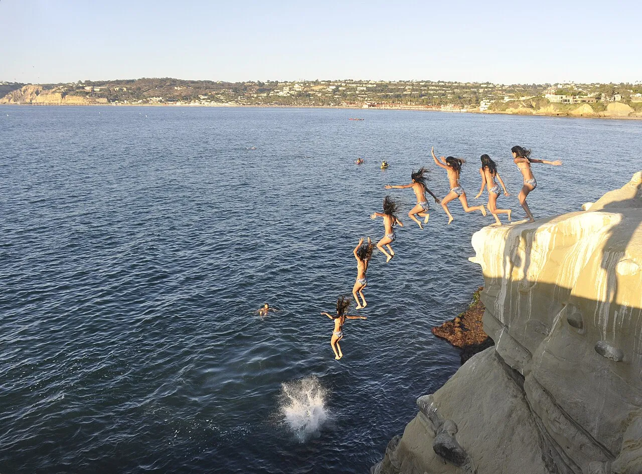 Cliff jumping near the big cave at La Jolla Cove , with La Jolla Shores in the background.