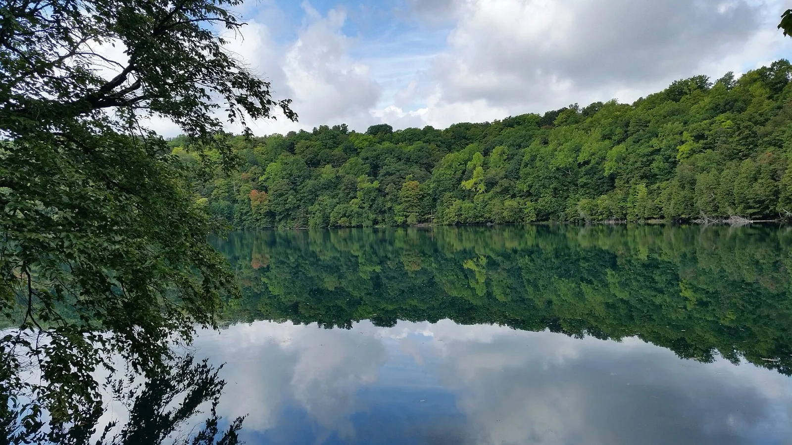 Wooded shoreline mirrored in Round Lake at Green Lakes State Park