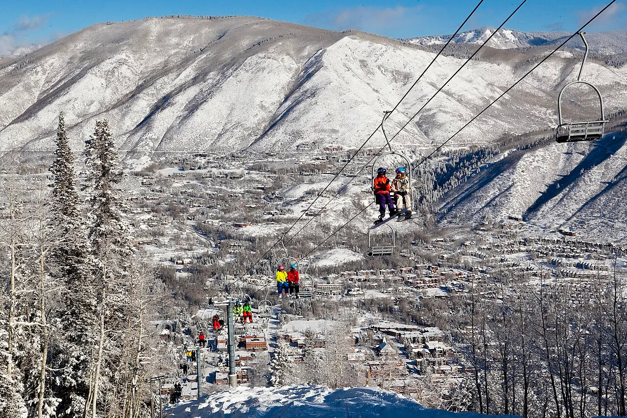 Skiers and snowboarders ride up the iconic Lift 1A on Aspen Mountain with downtown Aspen in the background.